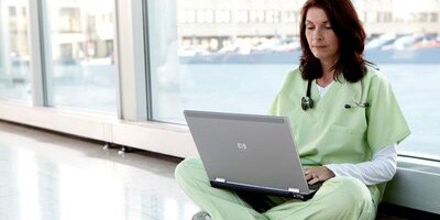 Female clinician sitting on the floor looking at her laptop
